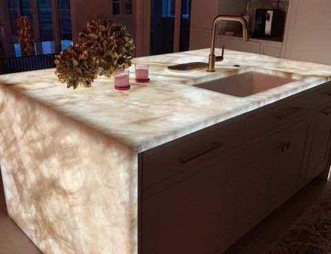 A kitchen island with an illuminated, translucent marble countertop and a sink, set in a modern home.