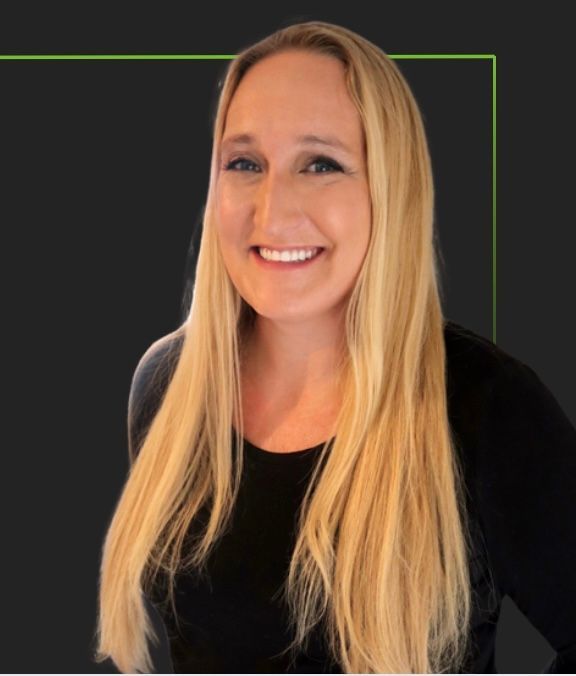 Blonde woman with long hair smiles at the camera, wearing a black top against a dark background.
