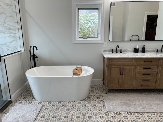 A bathroom with a bathtub , sink , mirror and window.