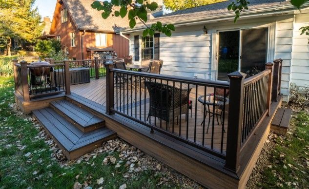 A large wooden deck with a black railing is in front of a house.