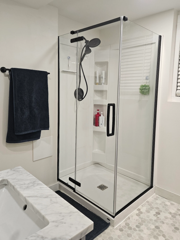Modern corner shower with black frame, glass doors, and rainfall showerhead next to a marble-topped bathroom vanity.