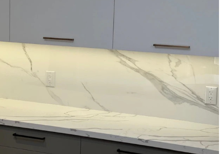 White marble backsplash with grey veining, featuring two wall outlets below light grey kitchen cabinets.