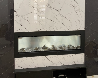 A modern, wide electric fireplace set into a white marble-patterned panel against a dark, textured wall.