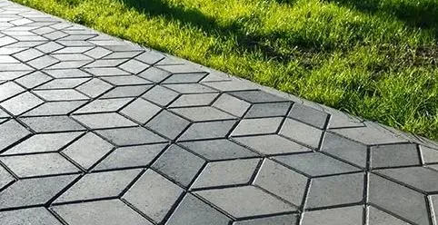 Gray geometric stone walkway beside bright green grass in sunlight