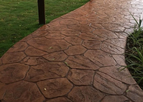Textured red stamped concrete walkway curving beside a grassy lawn and plants