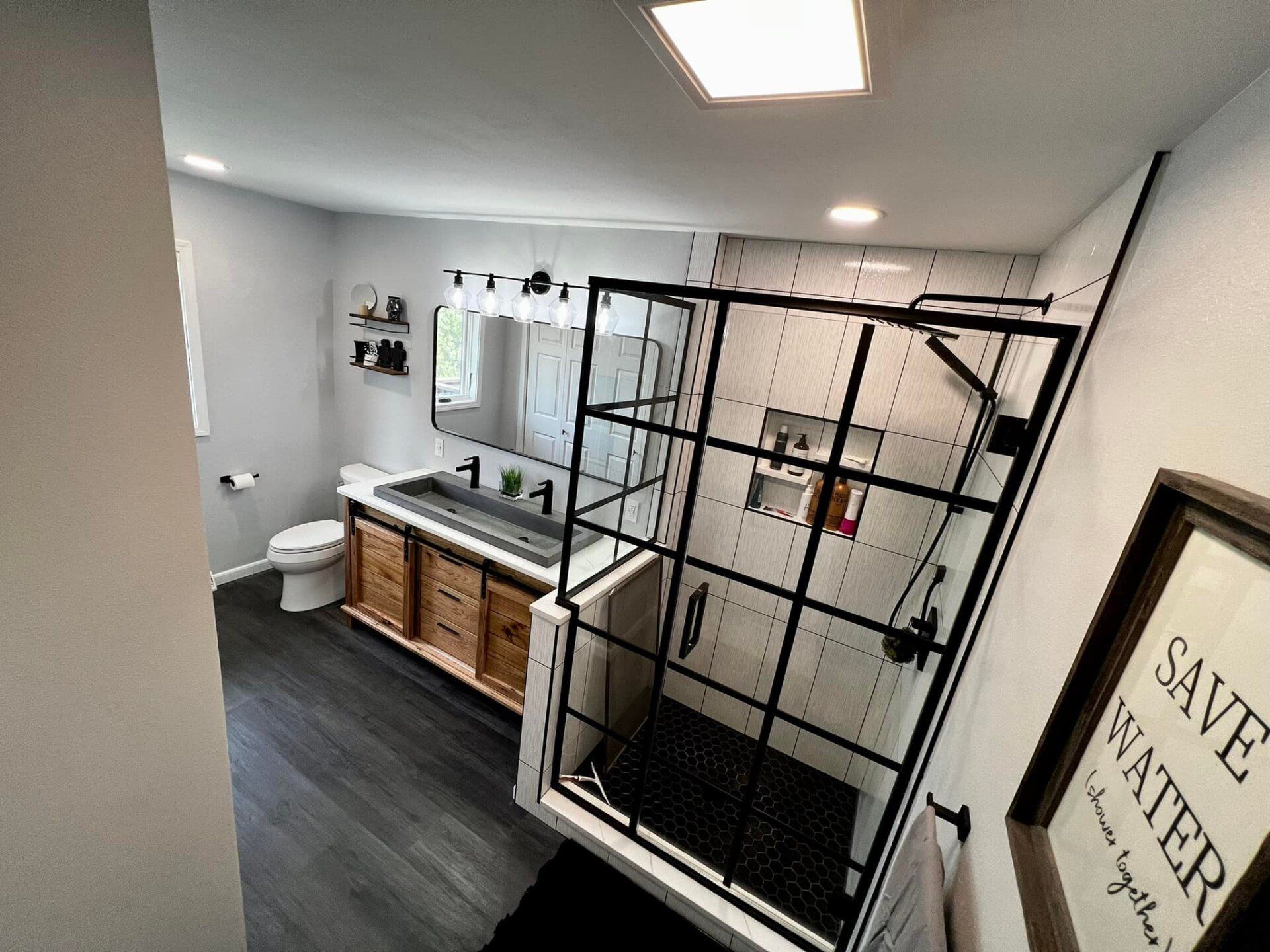 Modern bathroom with black framed shower, white tile, black and wood vanity, and dark floor.