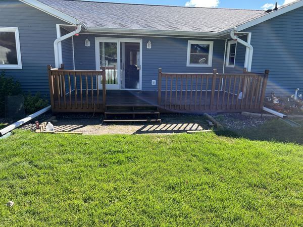 Wooden deck attached to a blue house with sliding glass door and steps leading to a green lawn.