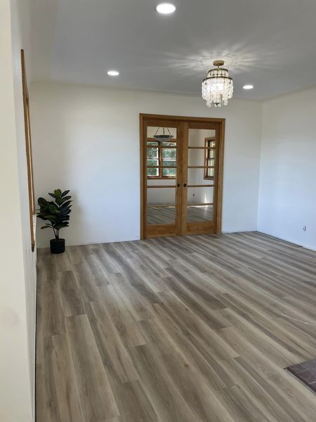Empty room with wood floors, French doors, and a chandelier.