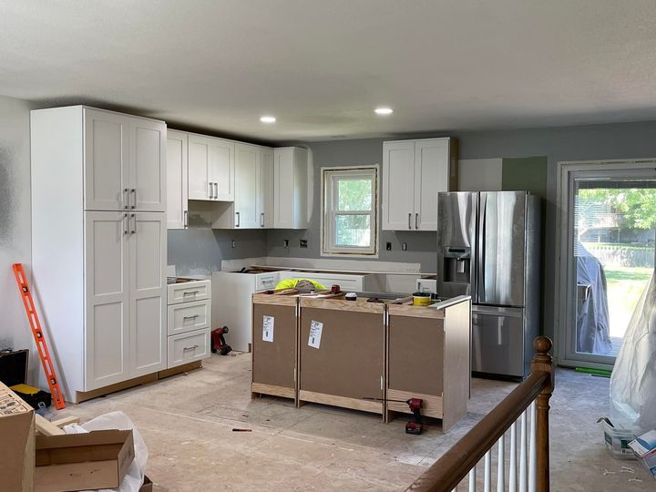 Kitchen under renovation with white cabinets, island, and stainless steel refrigerator.