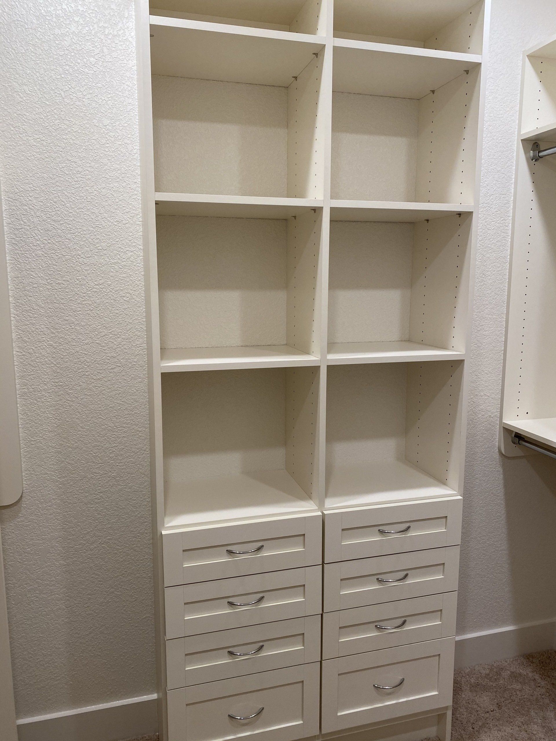 A walk in closet with white shelves and drawers.
