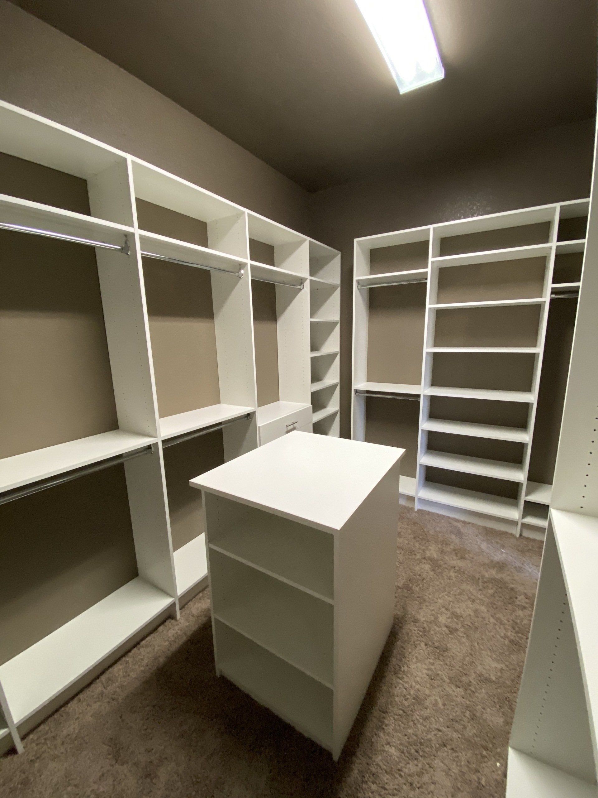 A walk in closet with lots of shelves and a table in the middle.