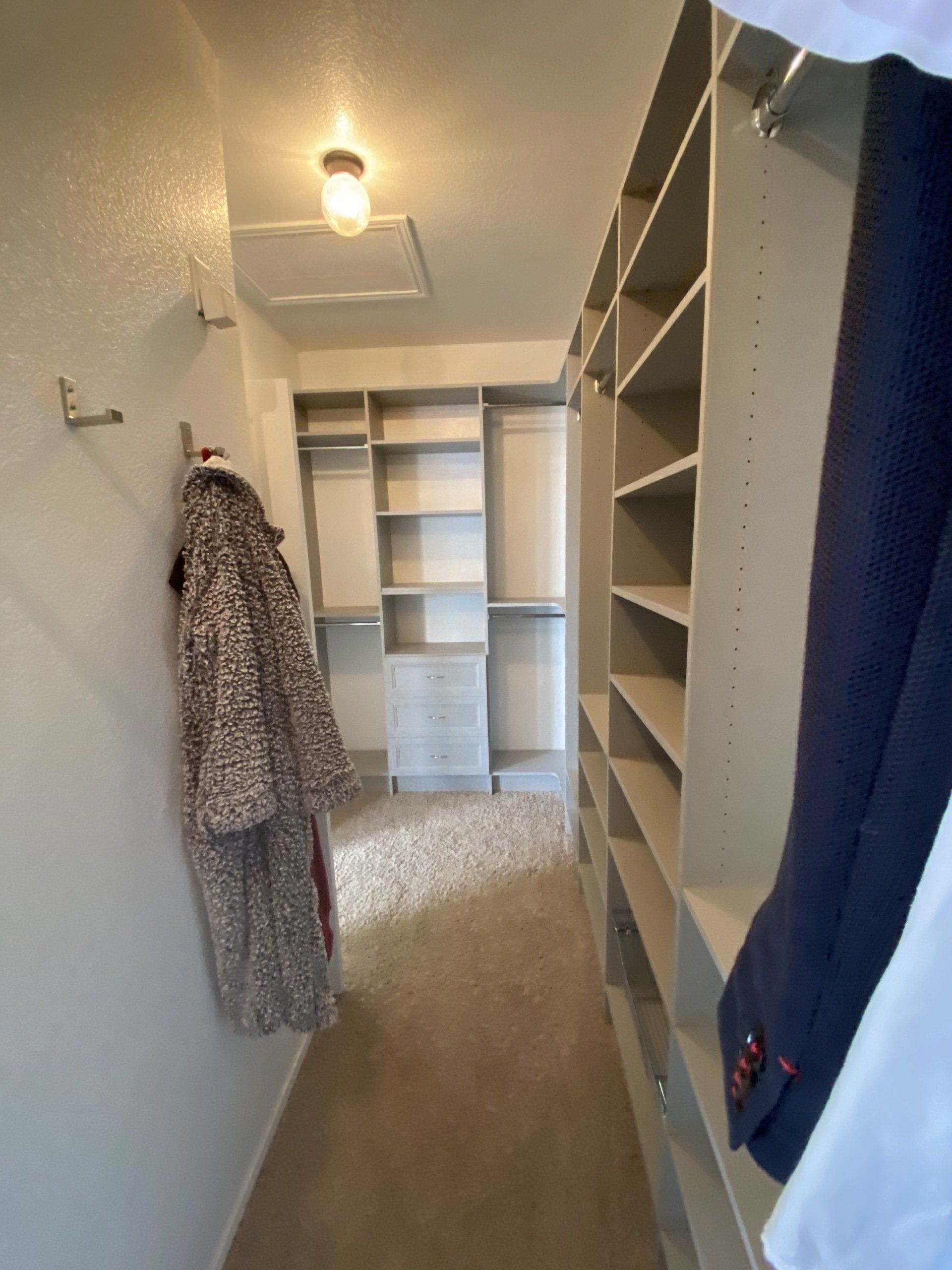 A walk in closet with a coat hanging on the wall