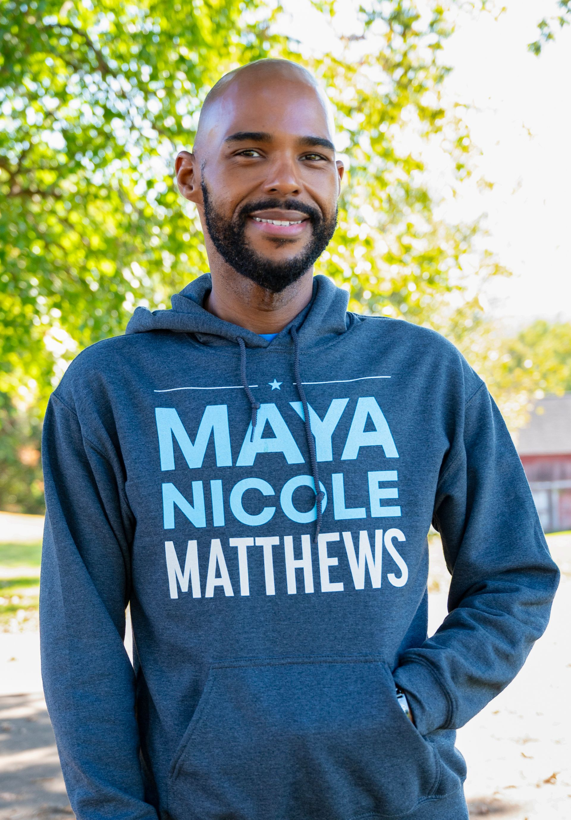 Man with a shaved head smiles, wearing a blue hoodie with 