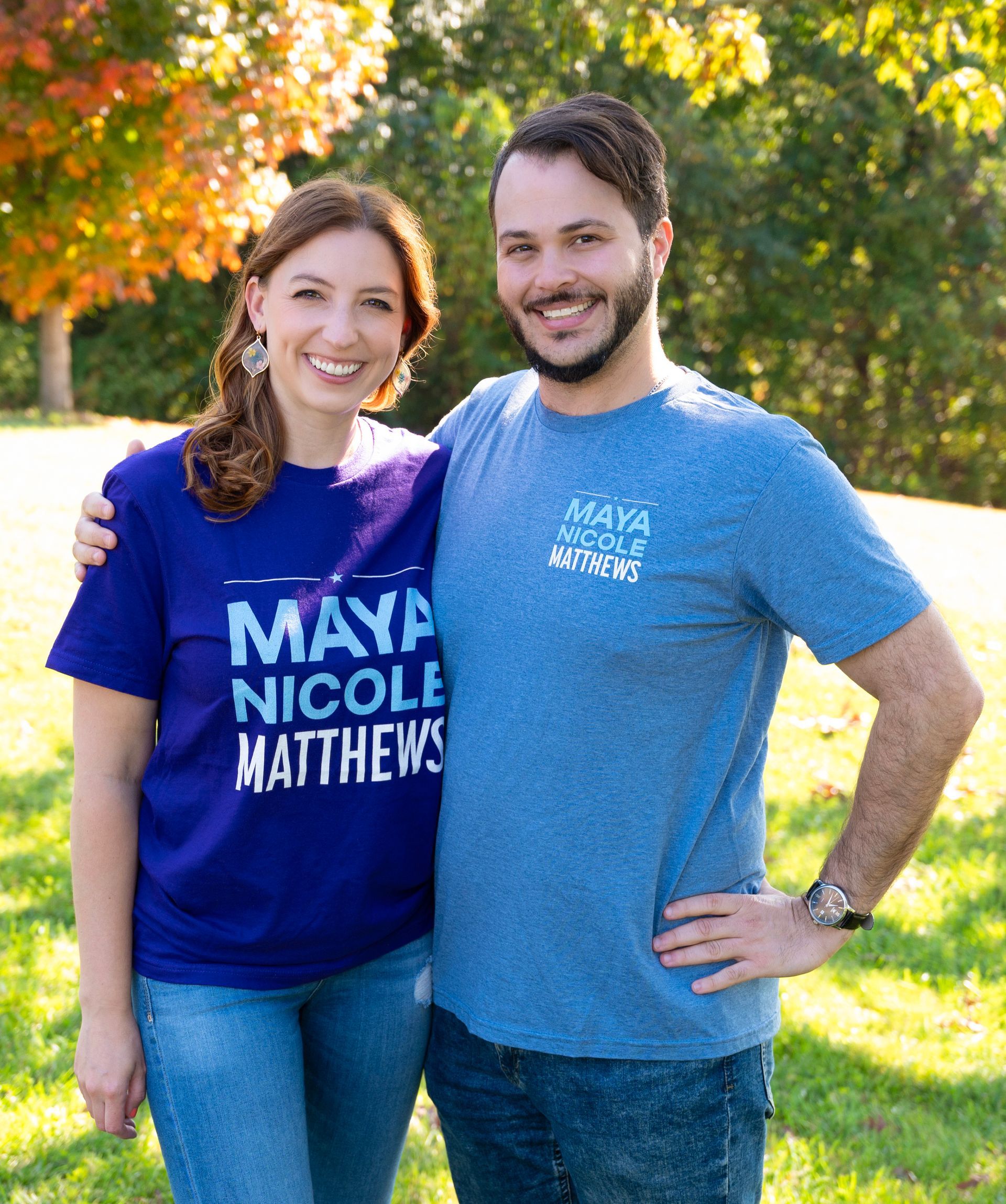 A woman in a campaign shirt and a man stand together smiling outdoors in front of a tree.