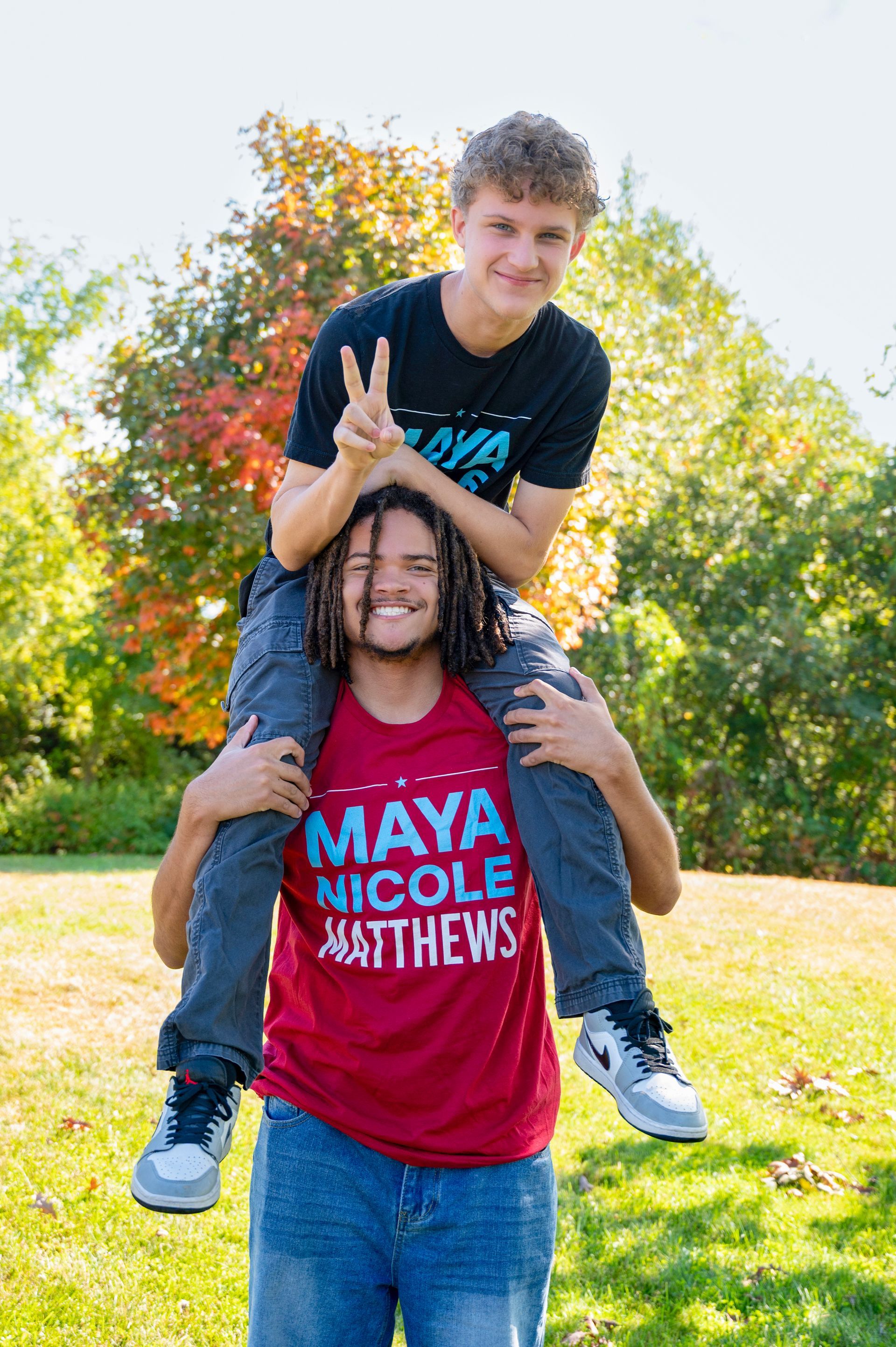 Two young men outdoors; one on the other's shoulders, smiling.