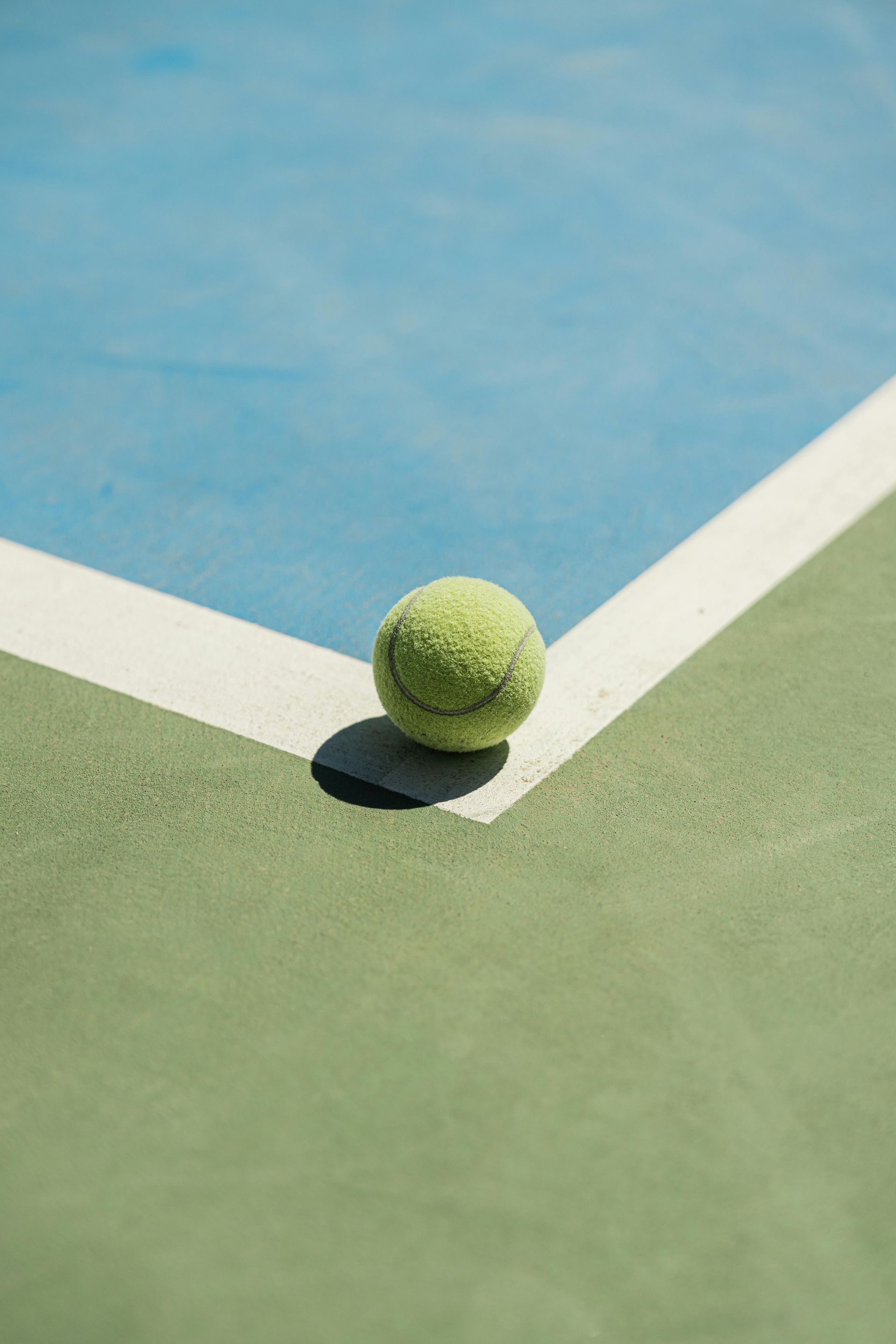 Tennis ball on the corner of a green and blue tennis court.