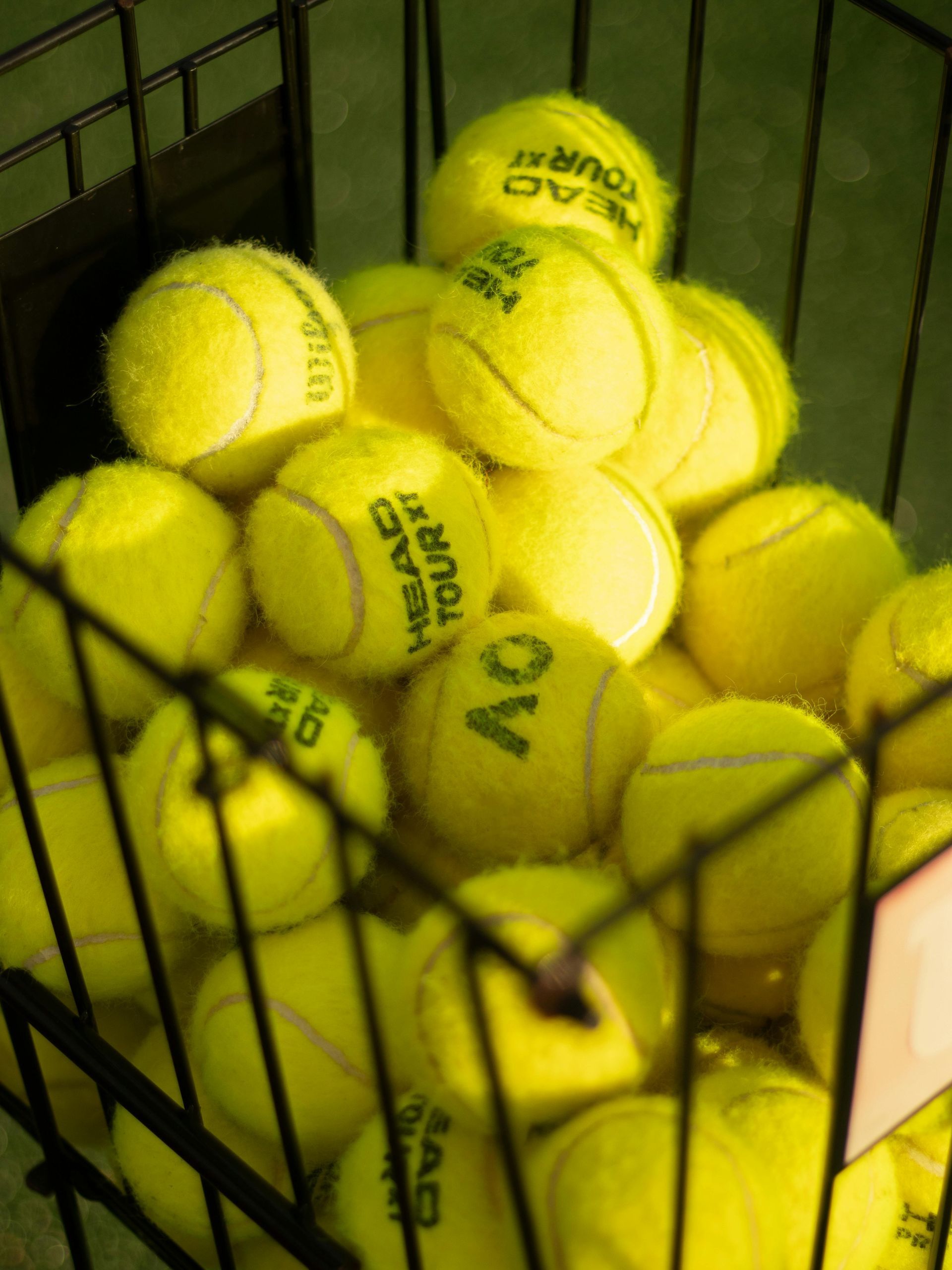 Yellow tennis balls stacked in a wire basket; some balls show 
