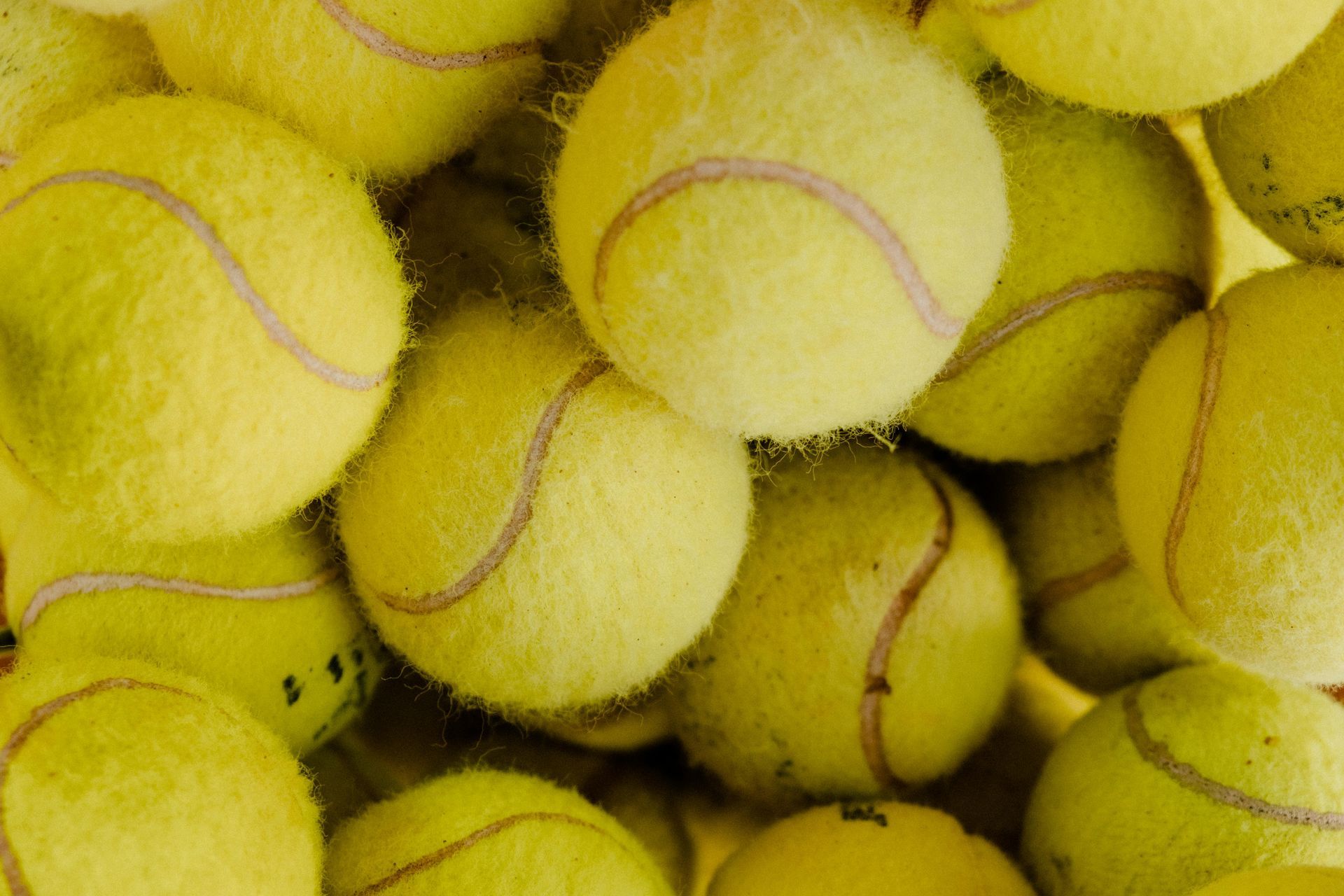 Pile of yellow tennis balls, tightly packed together, showing the fuzzy texture and curved seams.