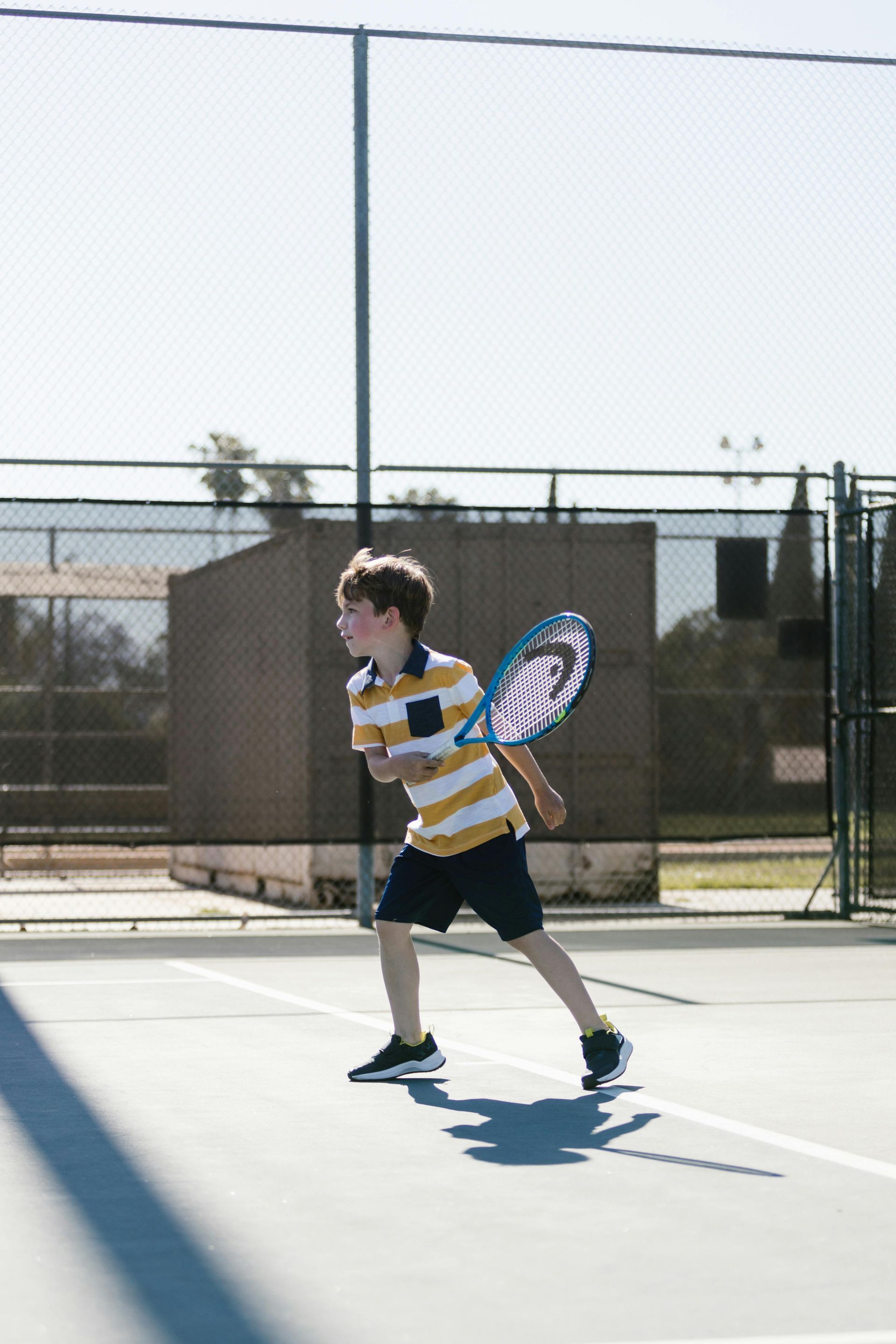 Boy in yellow shirt playing tennis on a blue court.