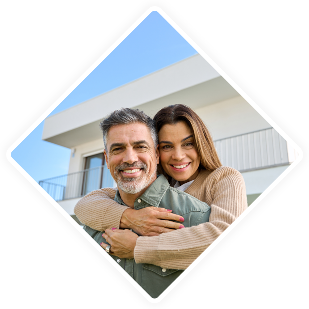 A man and a woman are hugging each other in front of a house.