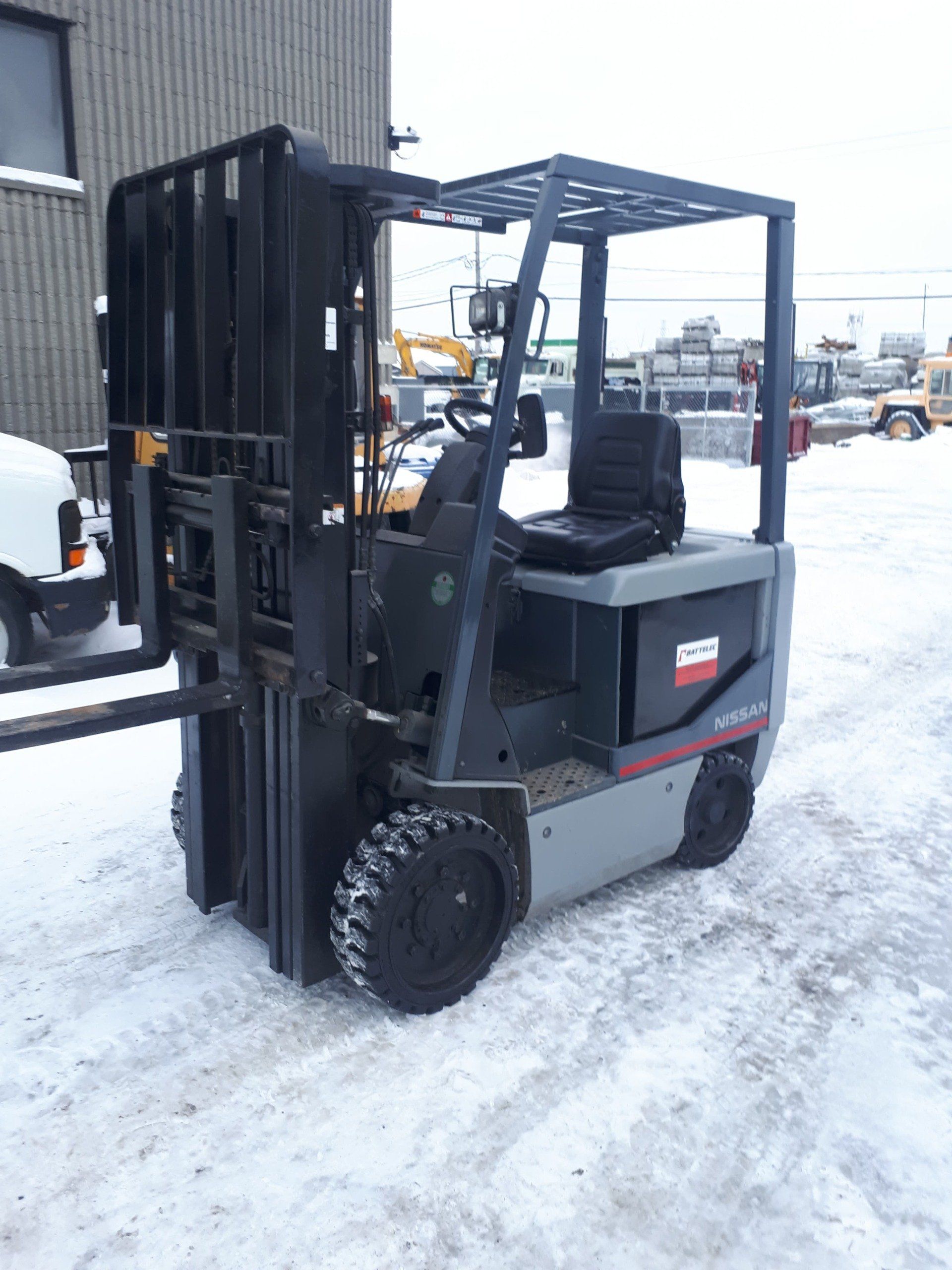 Chariot élévateur sur neige, gris et noir, avec fourches relevées, à l'extérieur.