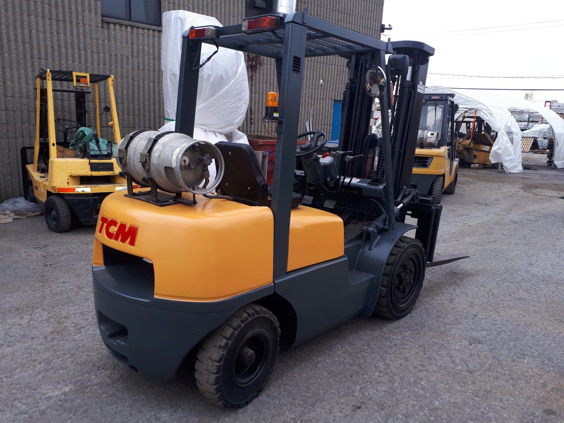 A yellow forklift with a gas tank on the back is parked in front of a building.
