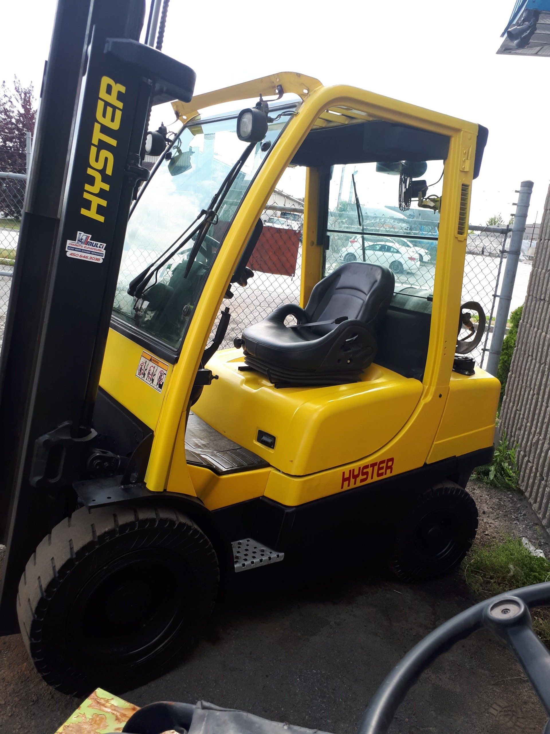 A yellow hyster forklift is parked in front of a chain link fence