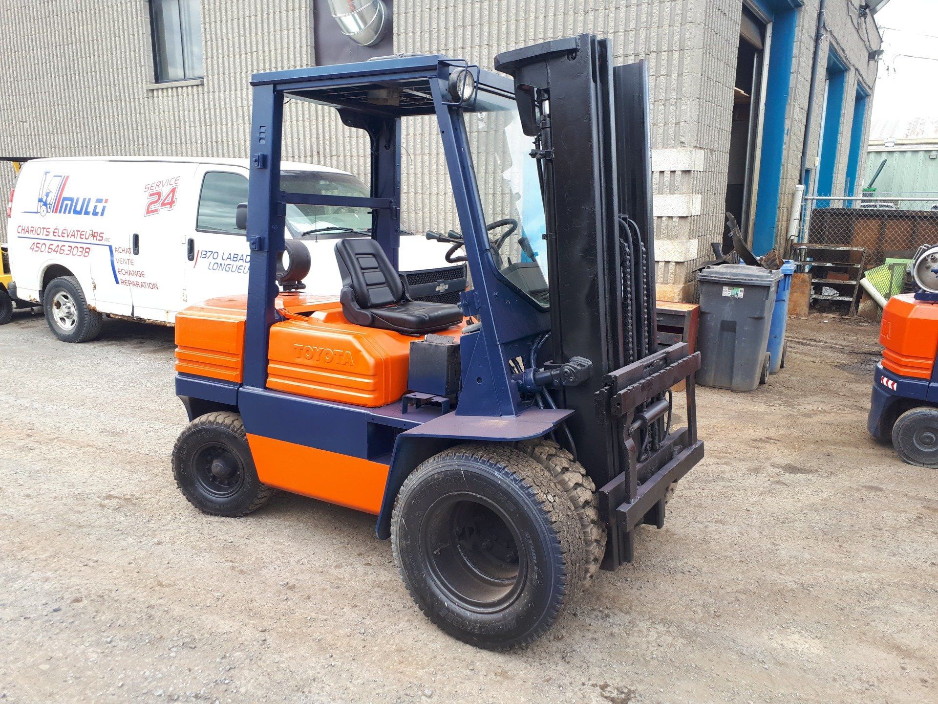 A blue and orange forklift is parked in front of a building.
