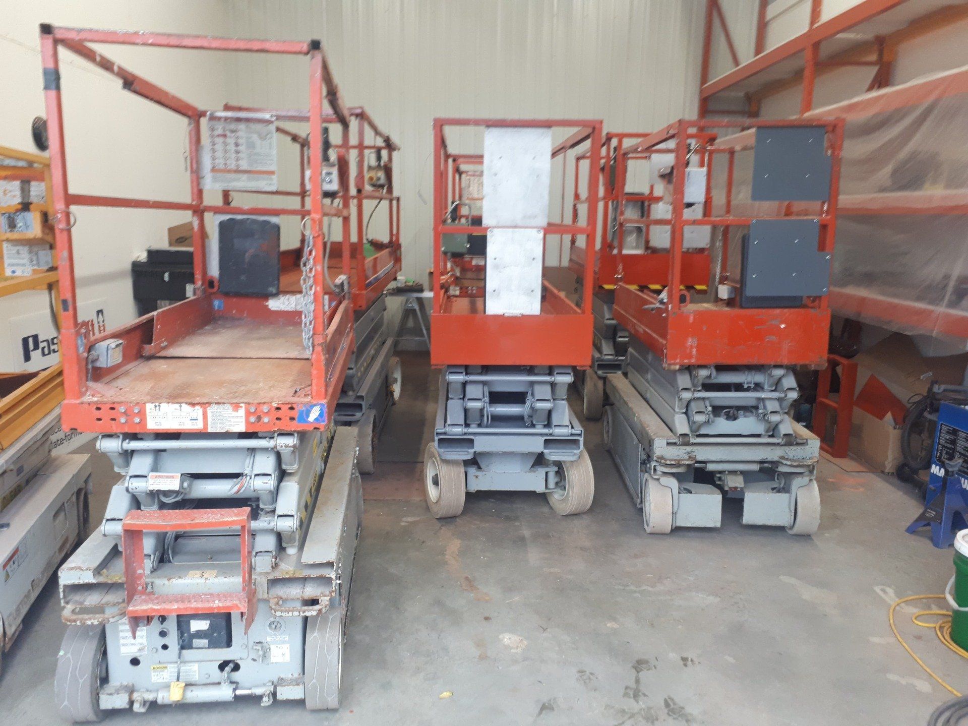 Three scissor lifts are lined up in a warehouse