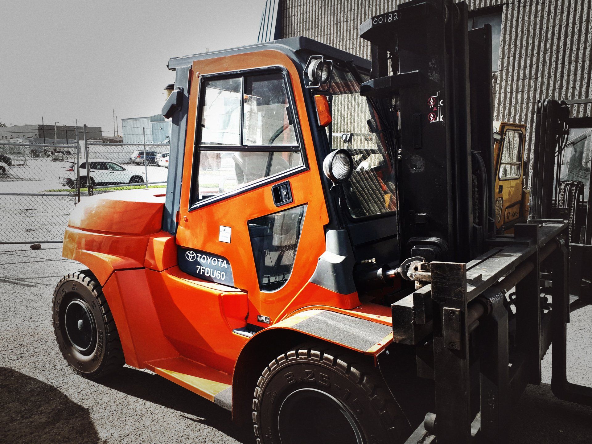 Chariot élévateur orange dans un décor extérieur avec un composant de levage de couleur sombre et un arrière-plan de bâtiment gris.
