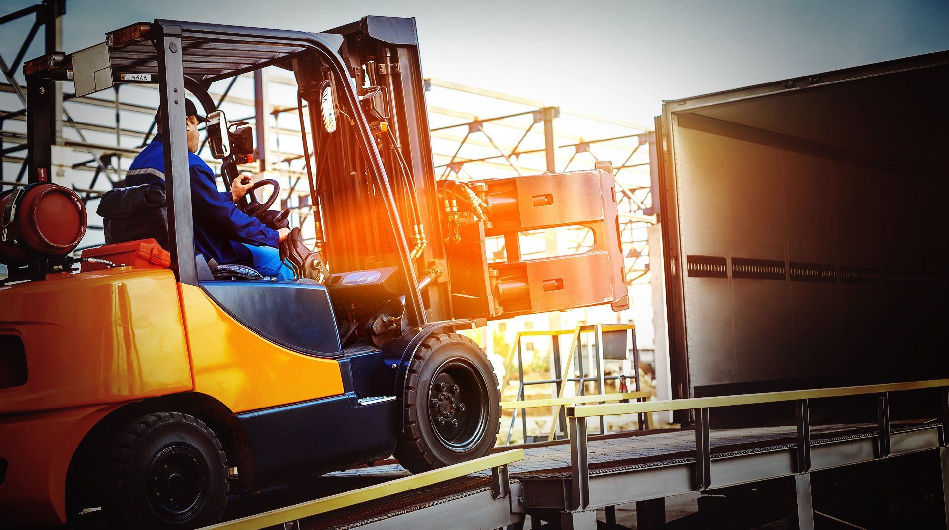Un chariot élévateur décharge un camion à un quai de chargement ; forte luminosité.