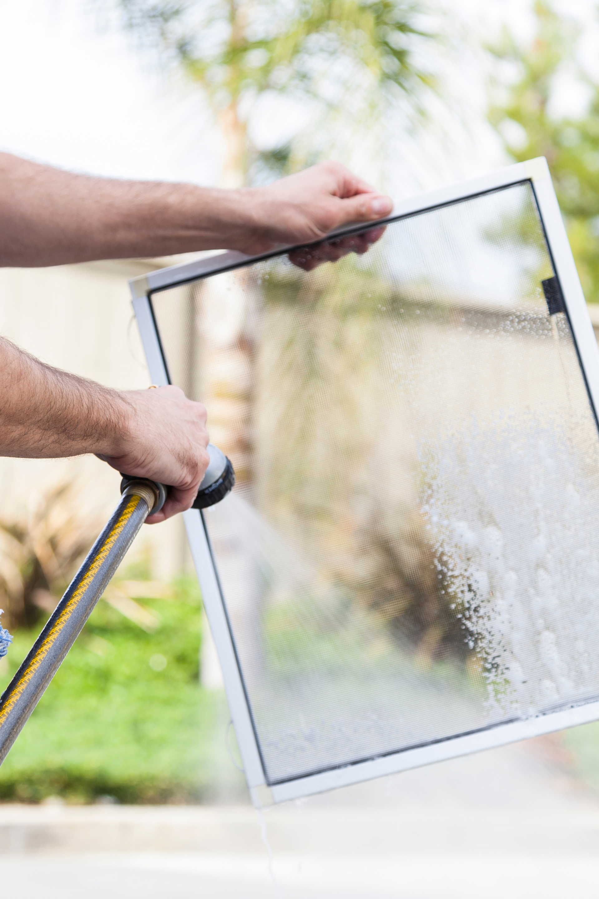 A man is cleaning a window screen with a hose.