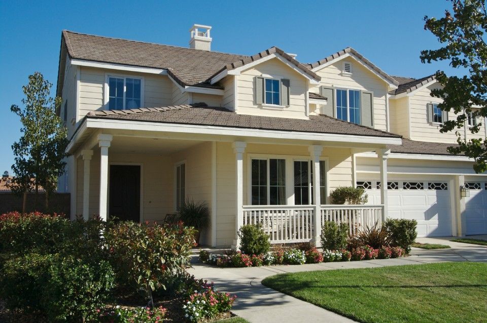 Two-story suburban house with beige siding, white trim, front porch, and manicured lawn