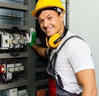 En man med hjälm och hörlurar arbetar på en elpanel.