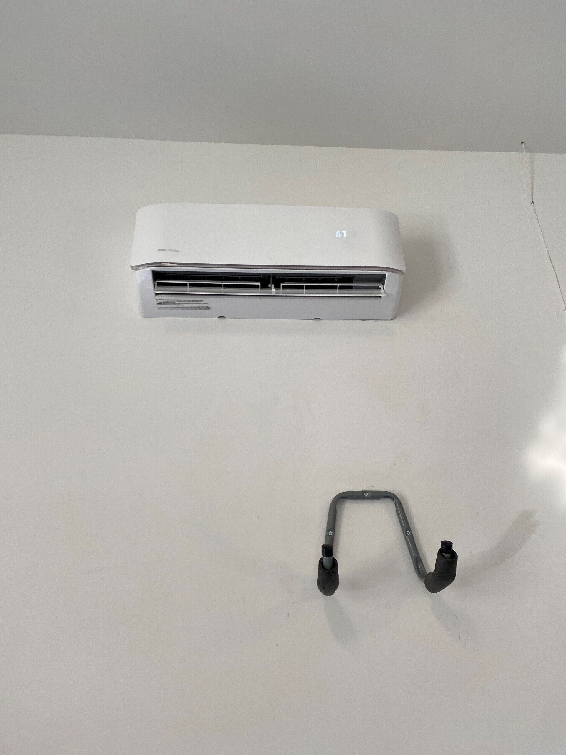 A white air conditioner is sitting on a white wall next to a hook.
