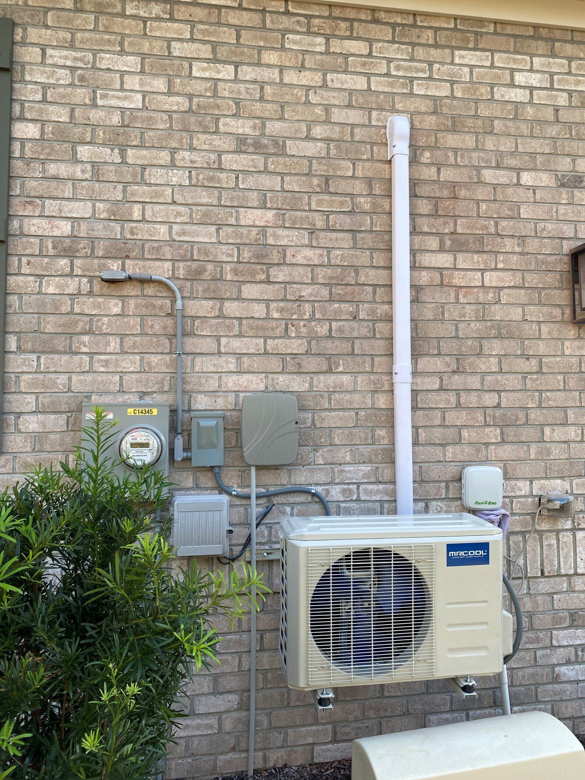 A white air conditioner is mounted on the side of a brick building.