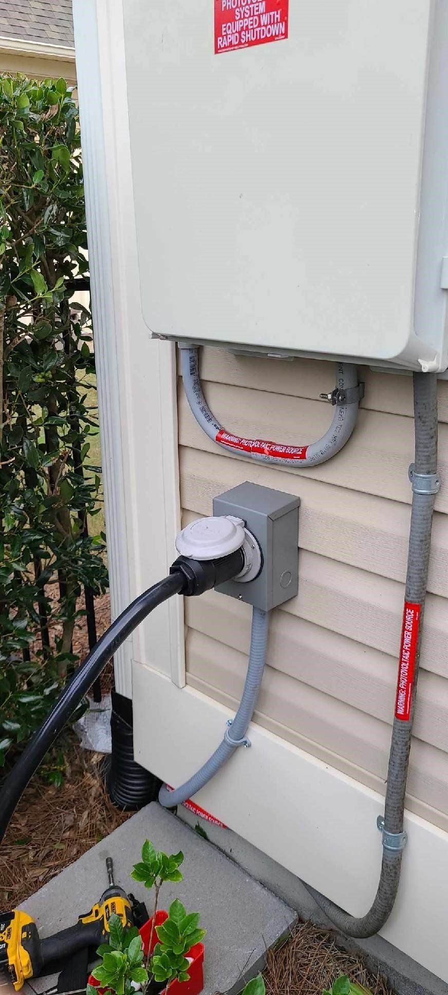 A power cord is plugged into a box on the side of a house.