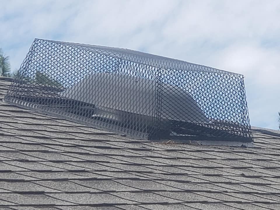 A chimney on top of a roof with a metal mesh covering it.