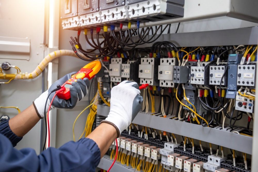 An electrician is working on an electrical panel with a multimeter.