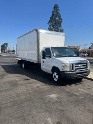 A white box truck parked on a paved lot under a clear blue sky.