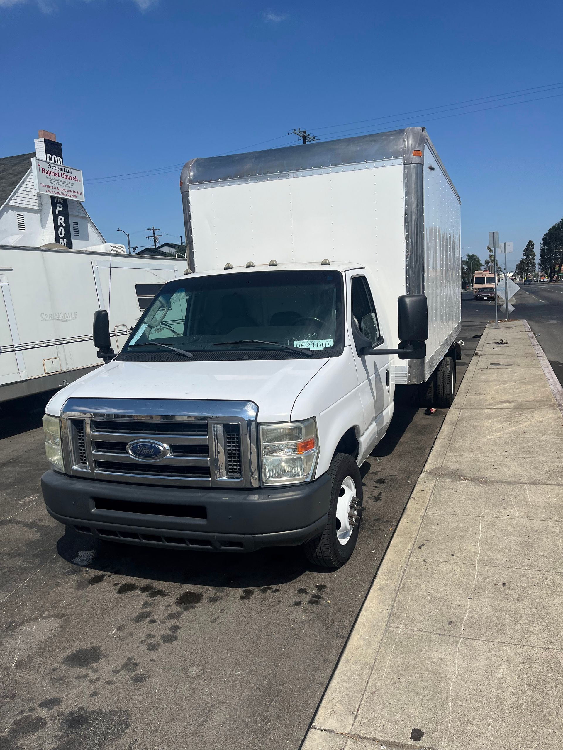A white box truck parked on a street next to a sidewalk under a clear blue sky.