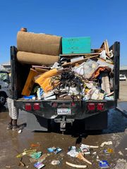 A person standing next to a truck bed filled with assorted junk and debris, with scattered trash on the ground.