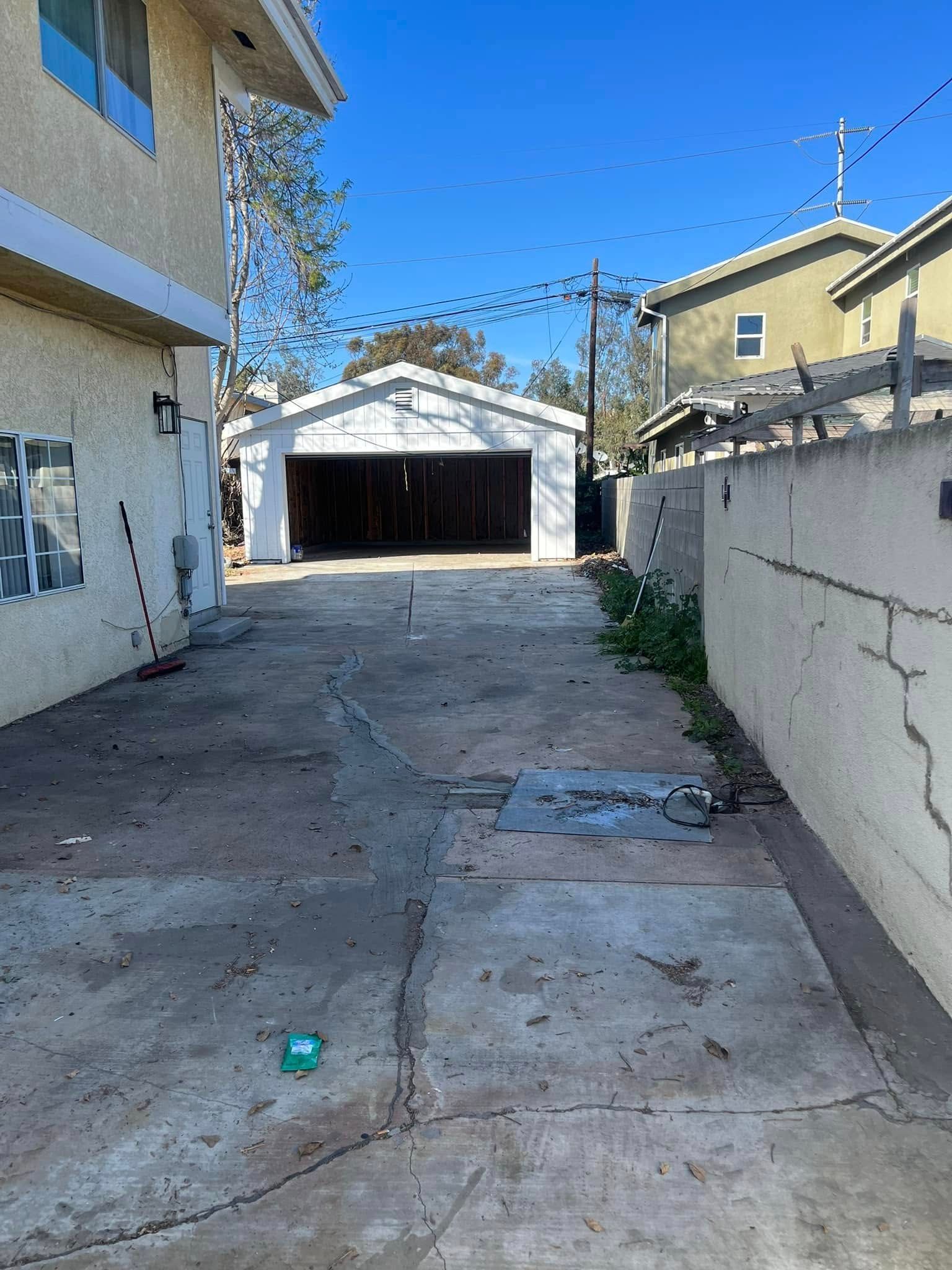 A concrete driveway leads toward a detached garage between two buildings under a clear blue sky.