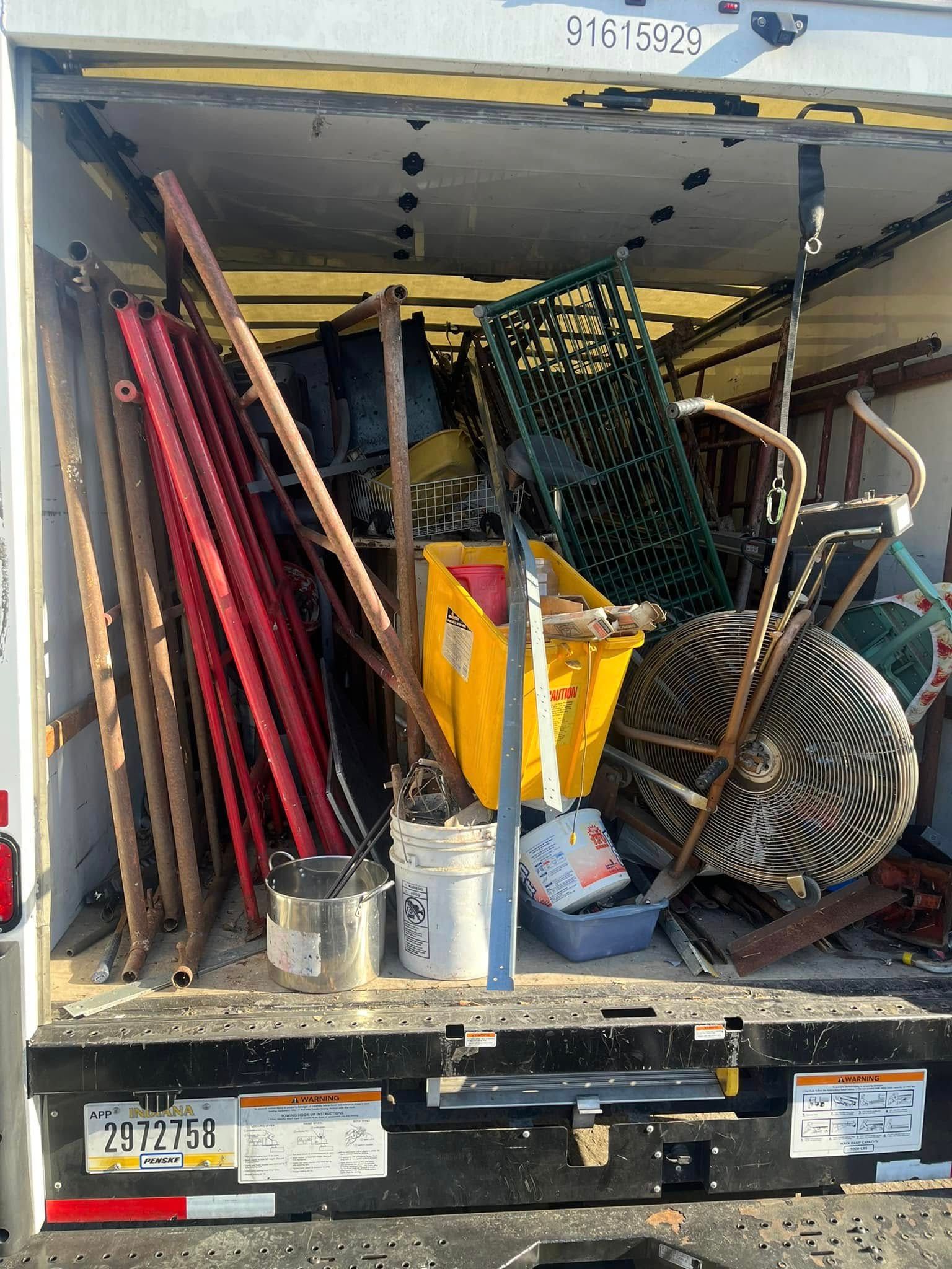 The open back of a moving truck packed with furniture, including red bed frames, a yellow bin, and a treadmill.