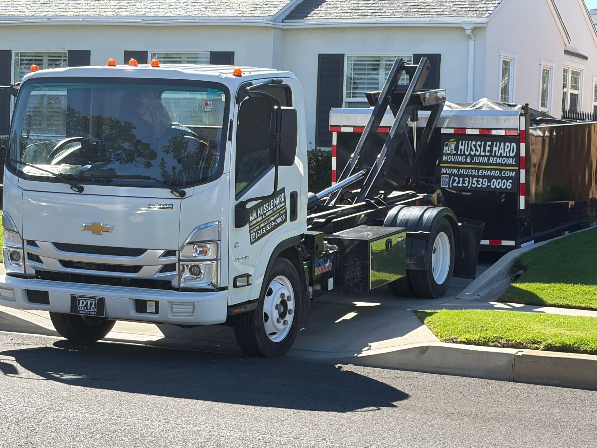 A white Chevrolet roll-off dump truck parked on a residential street in front of a house.