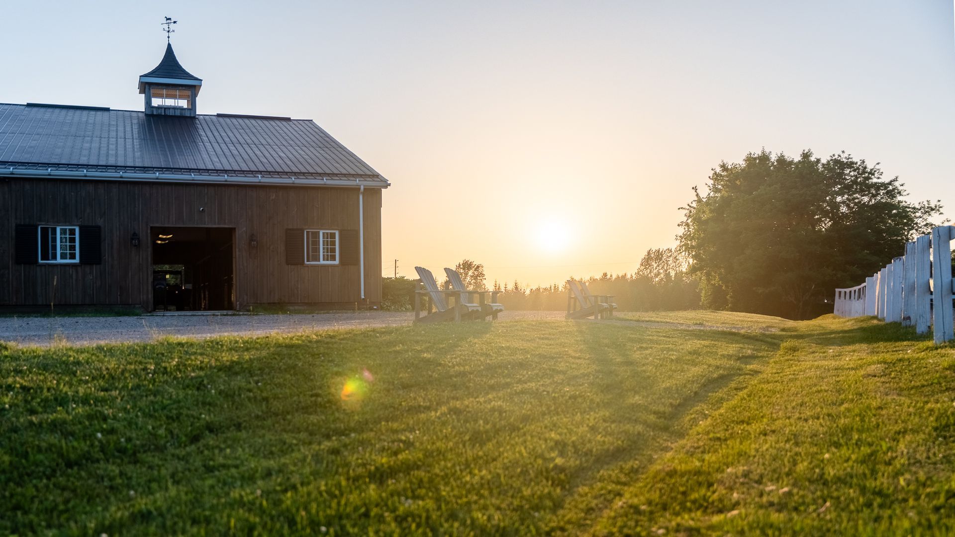 A barn is sitting in the middle of a grassy field at sunset.