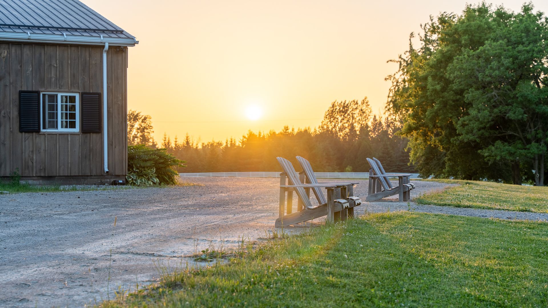 Two lawn chairs are sitting in front of a barn at sunset.