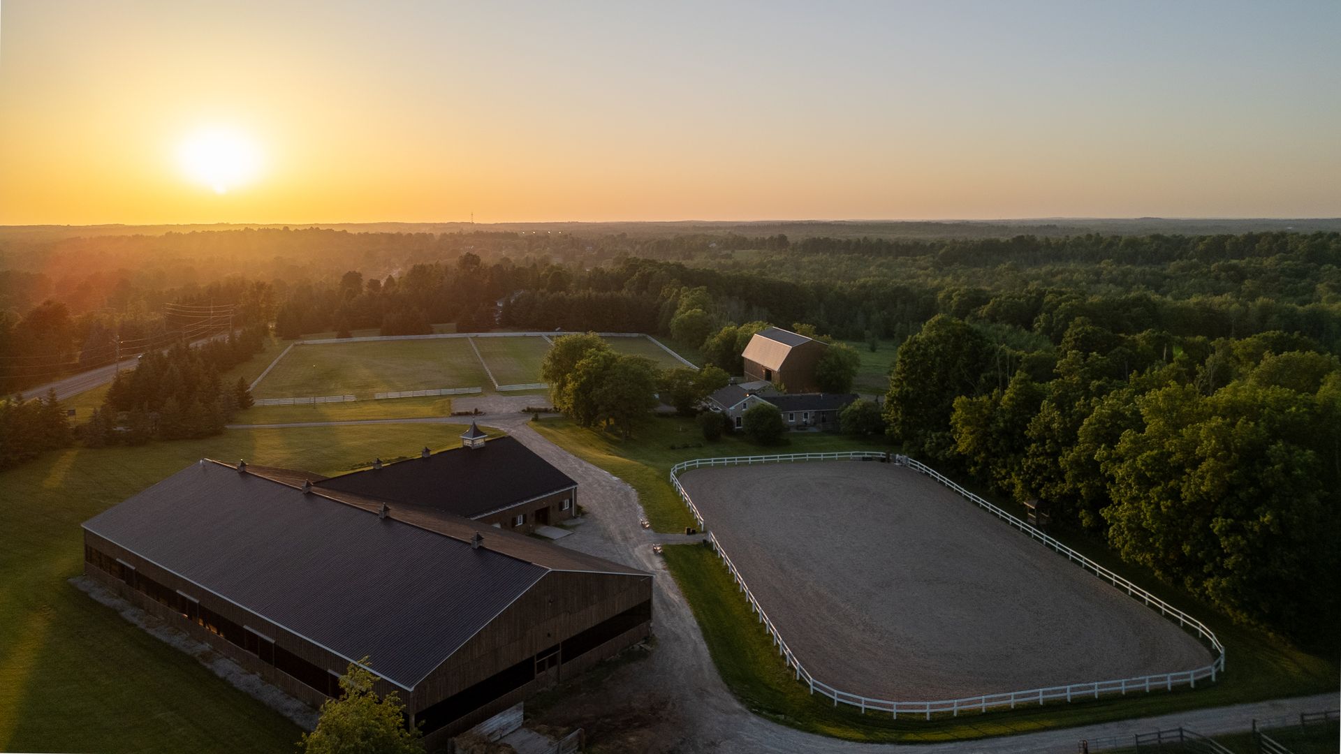 An aerial view of a horse farm with a sunset in the background.