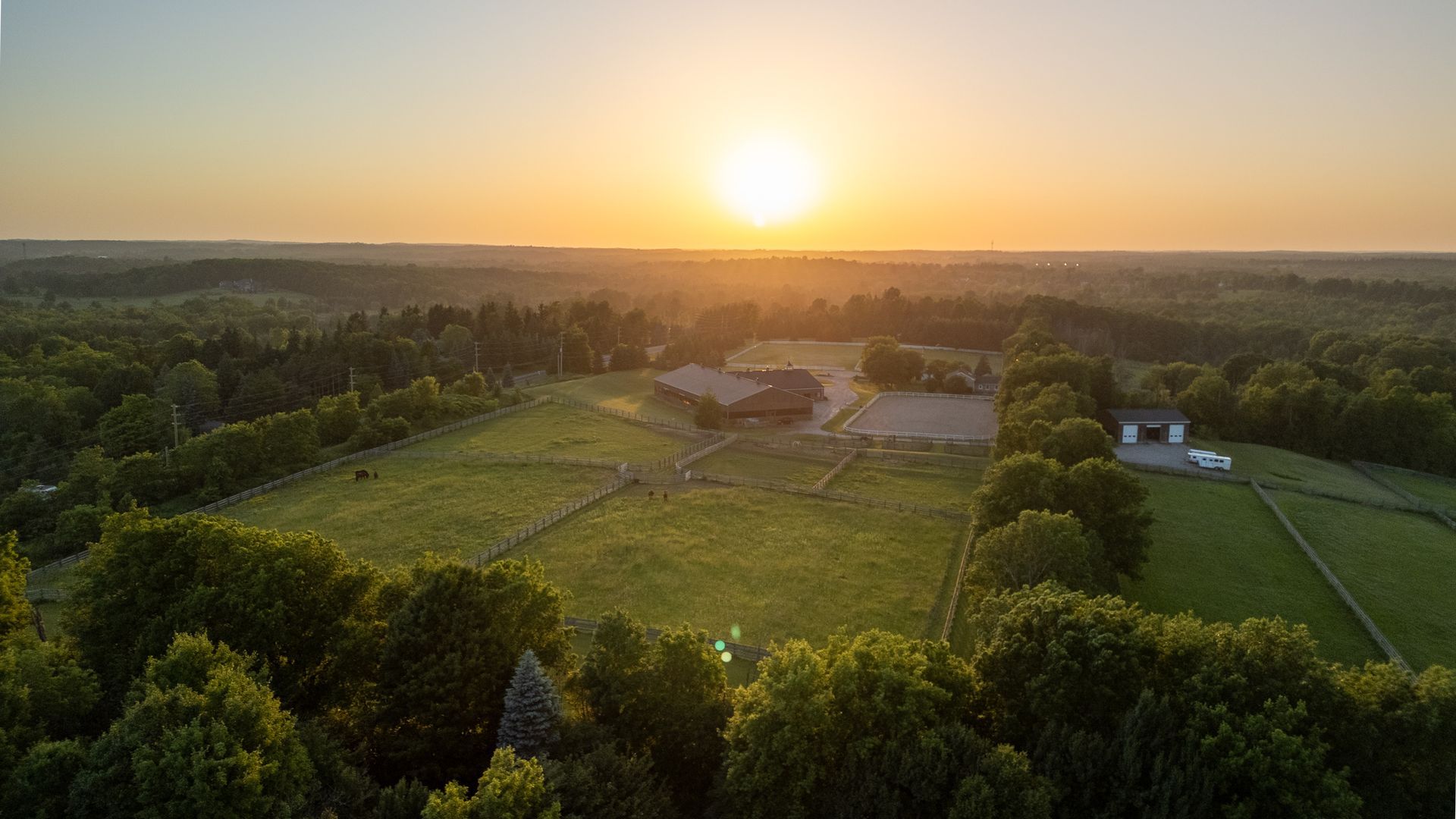 An aerial view of a farm at sunset with a barn in the distance.