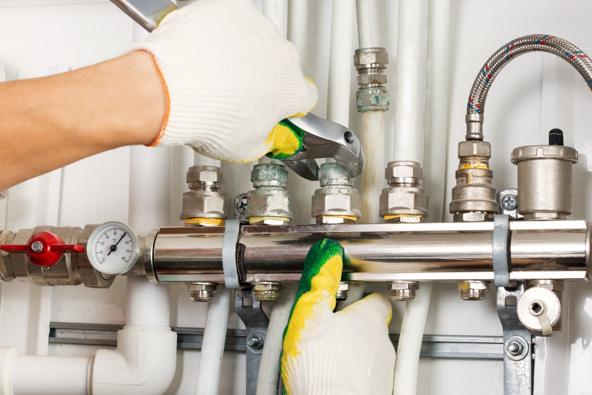 Gloved hands adjusting valves on a stainless steel pipe assembly with pressure gauges and hoses